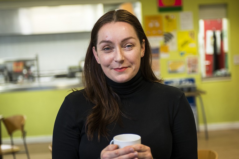 person smiling into the camea with a cup of tea